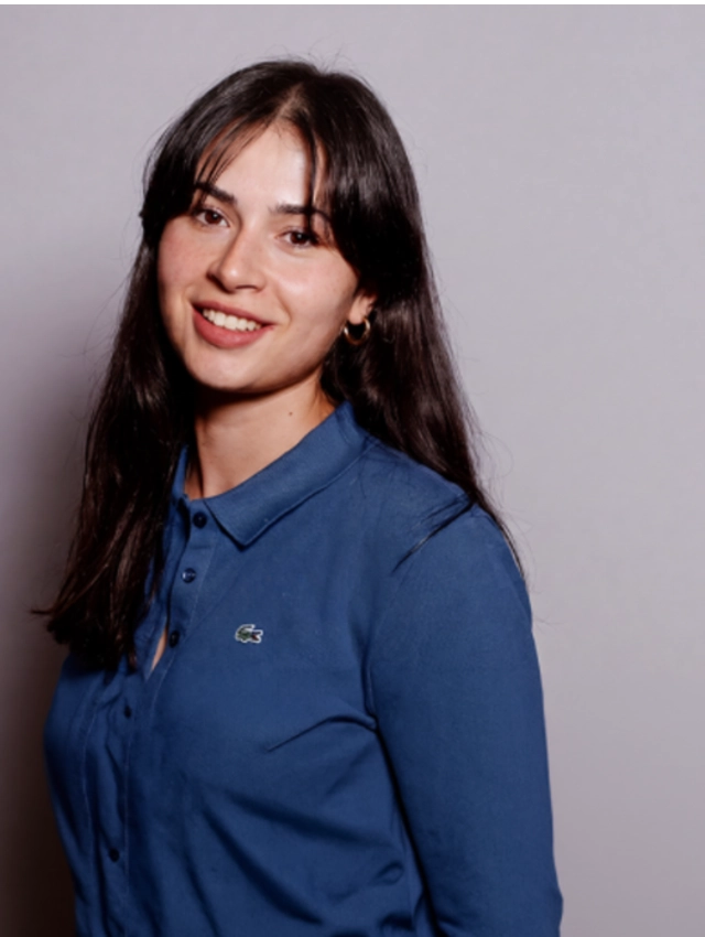 Studio-style portrait of person in blue collared shirt smiling
