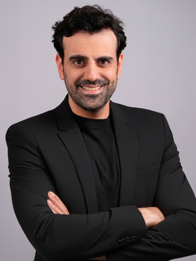 Person in black suit smiling against plain background