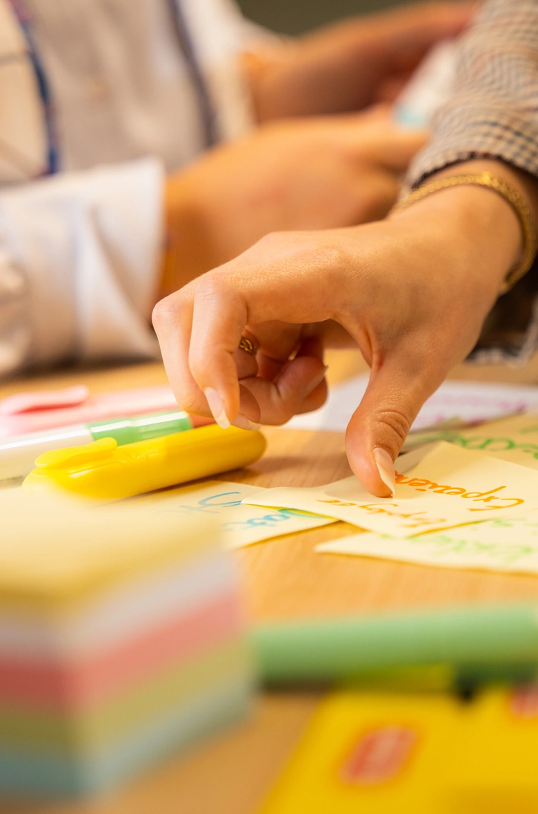 Hand pakt post-it tussen stiften op tafel.