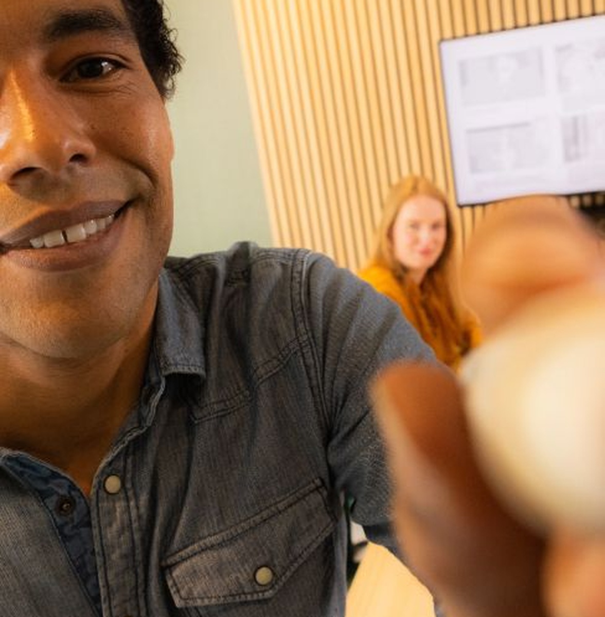 Persoon maakt selfie, collega en scherm op achtergrond