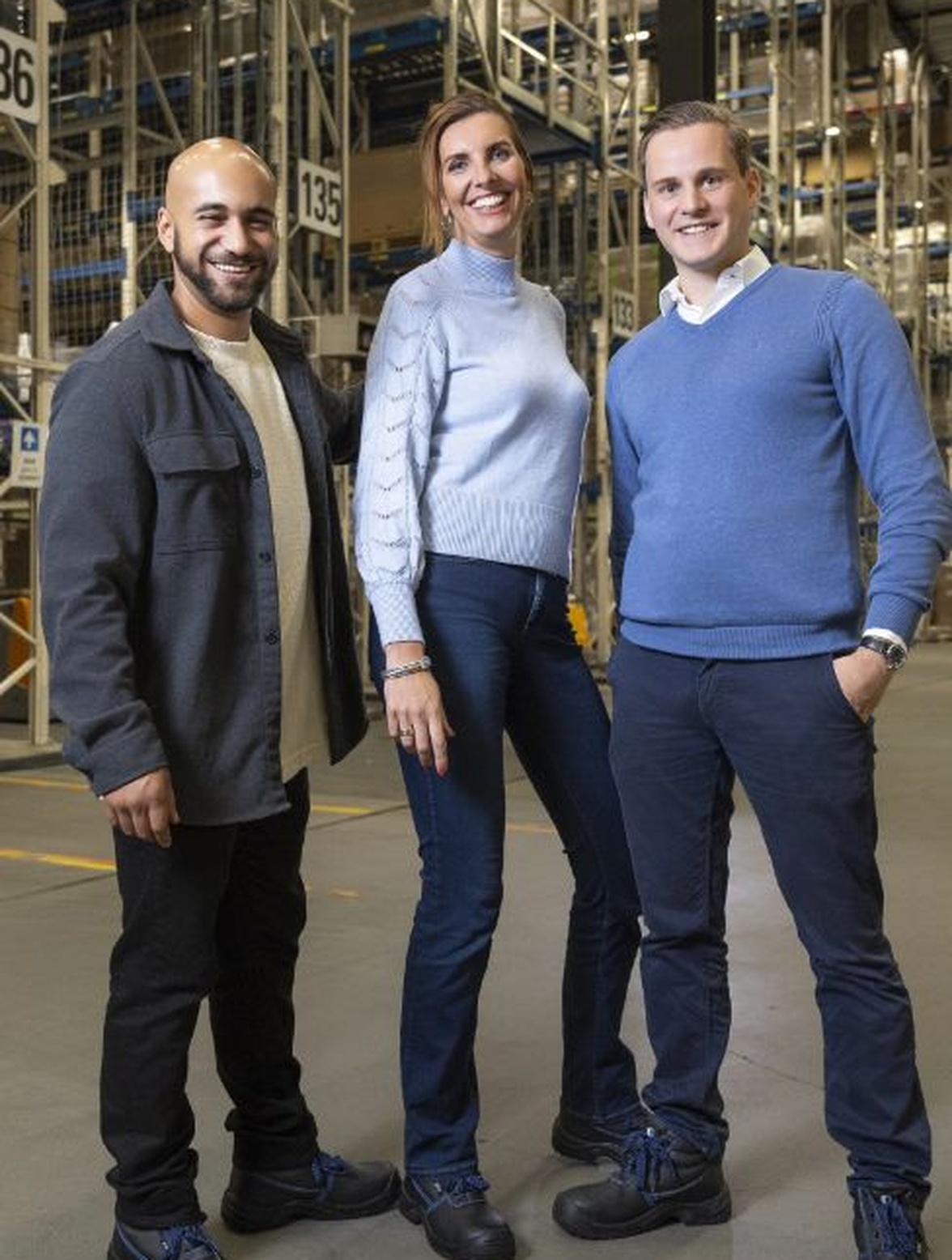 Drie mensen staan in een gangpad van een magazijn