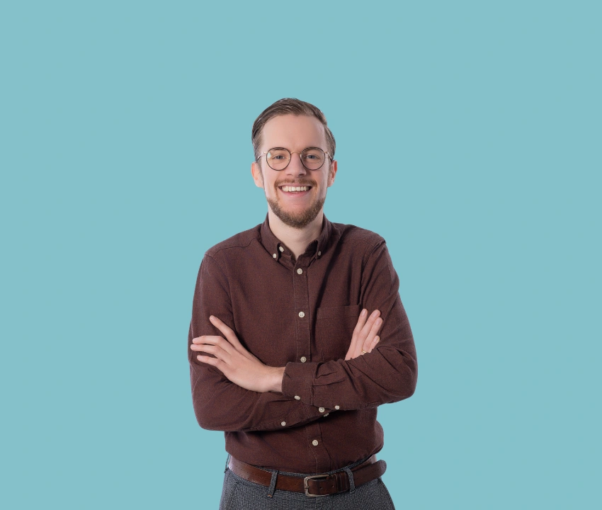 Persoon met bril en gevouwen armen poseert voor een effen lichtblauwe achtergrond in een portretfoto