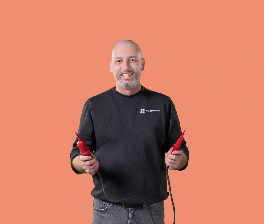 Persoon in werkkleding houdt twee geïsoleerde testpennen vast en poseert voor een effen oranje achtergrond.