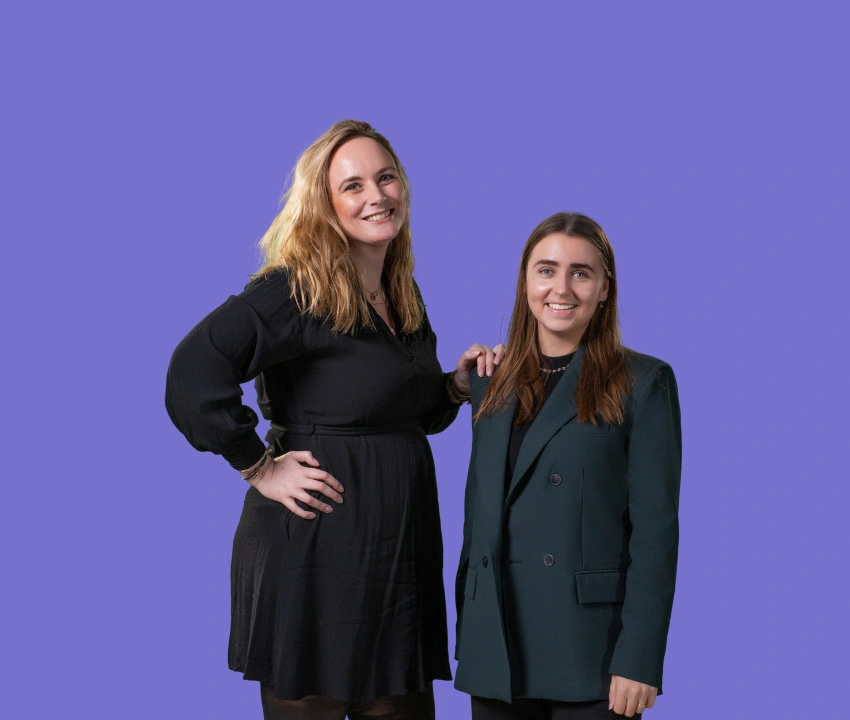 Twee personen poseren naast elkaar voor een effen paarse achtergrond in een studioportret.