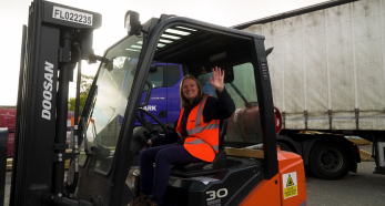 Person waving from forklift beside delivery truck