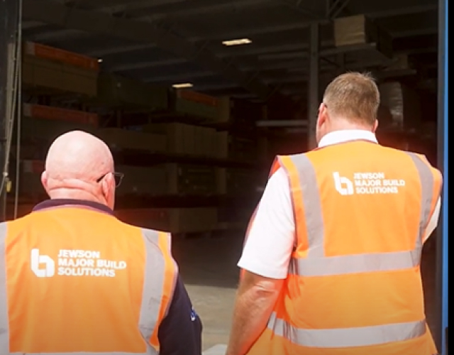 Two workers in safety vests entering warehouse