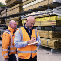 Workers inspect timber stock in outdoor storage.