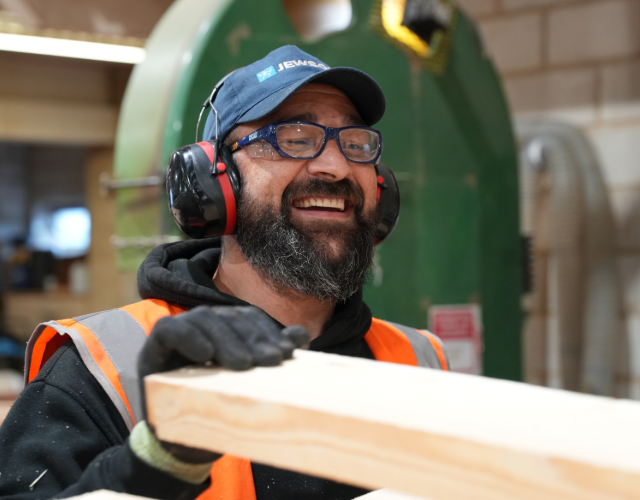 Forklift operator in hi-vis vest waving to camera