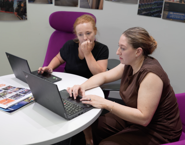 Two colleagues collaborating on laptops in office