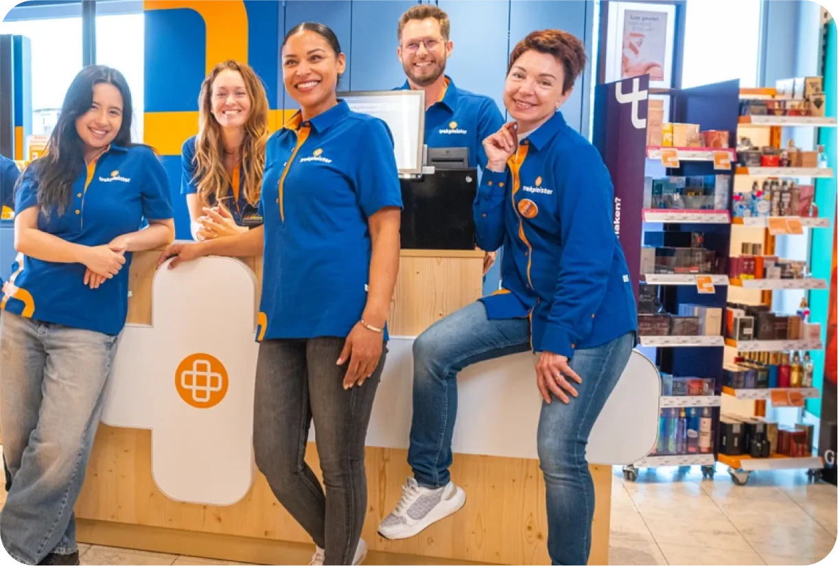 Four retail employees in blue uniforms smiling and posing behind a store counter.