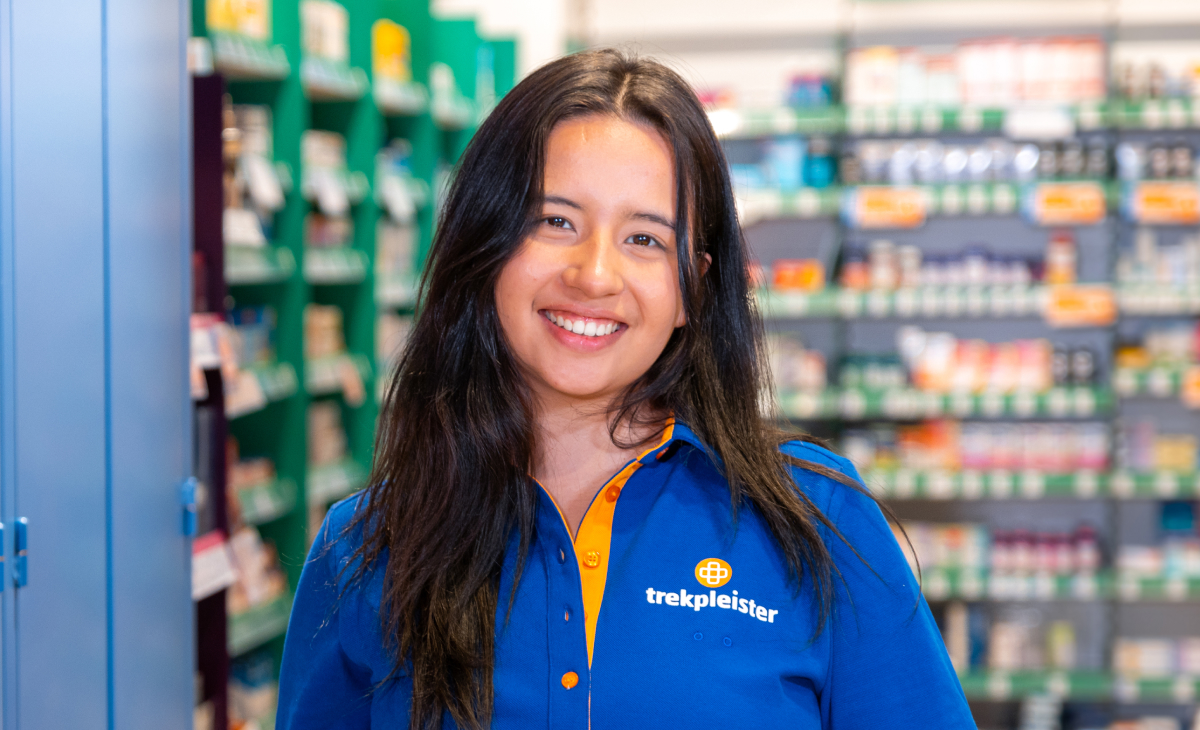 Medewerker in een blauwe Trekpleister-uniform poseert in een drogisterijwinkel.